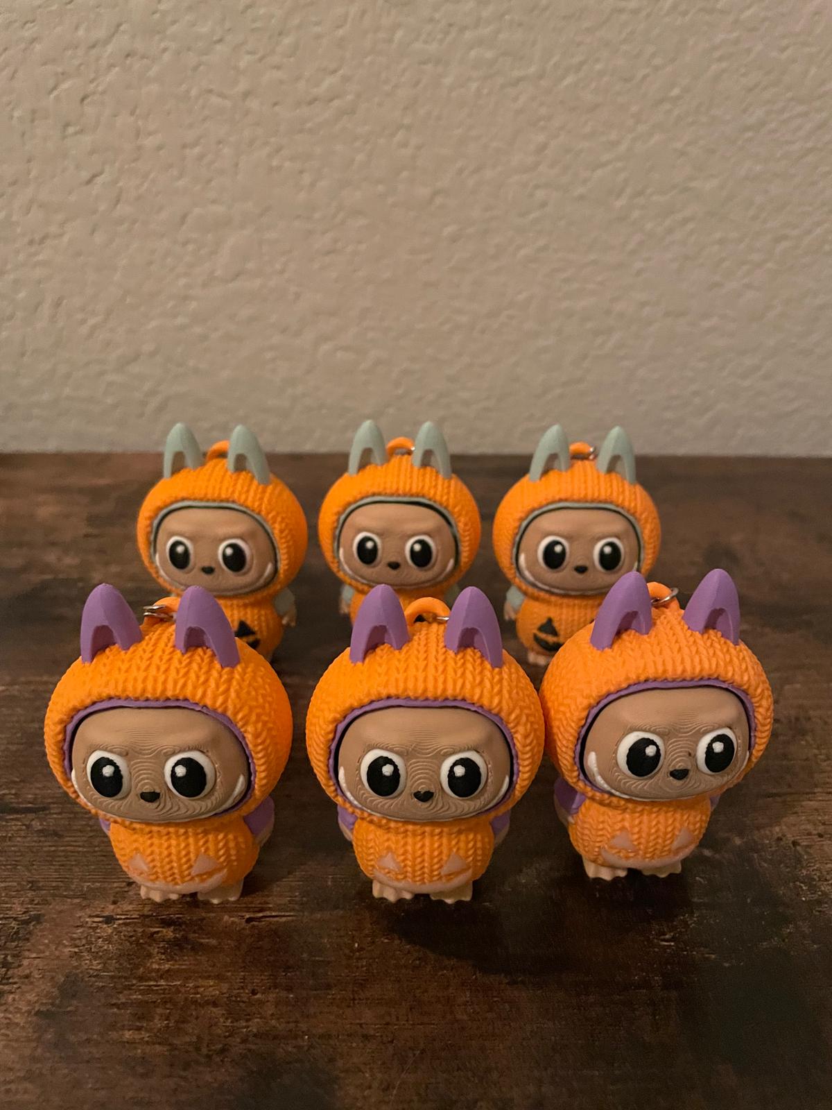 Limited edition Halloween Labubu fidget toy in a pumpkin onesie outfit with jack-o’-lantern details. Cute collectible figure with a clicky face feature, designed for Halloween season décor, stress relief, and toy collectors.