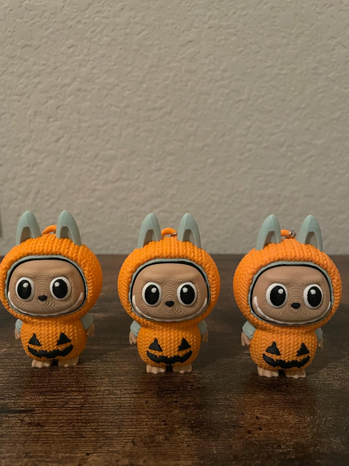 Limited edition Halloween Labubu fidget toy in a pumpkin onesie outfit with jack-o’-lantern details. Cute collectible figure with a clicky face feature, designed for Halloween season décor, stress relief, and toy collectors.