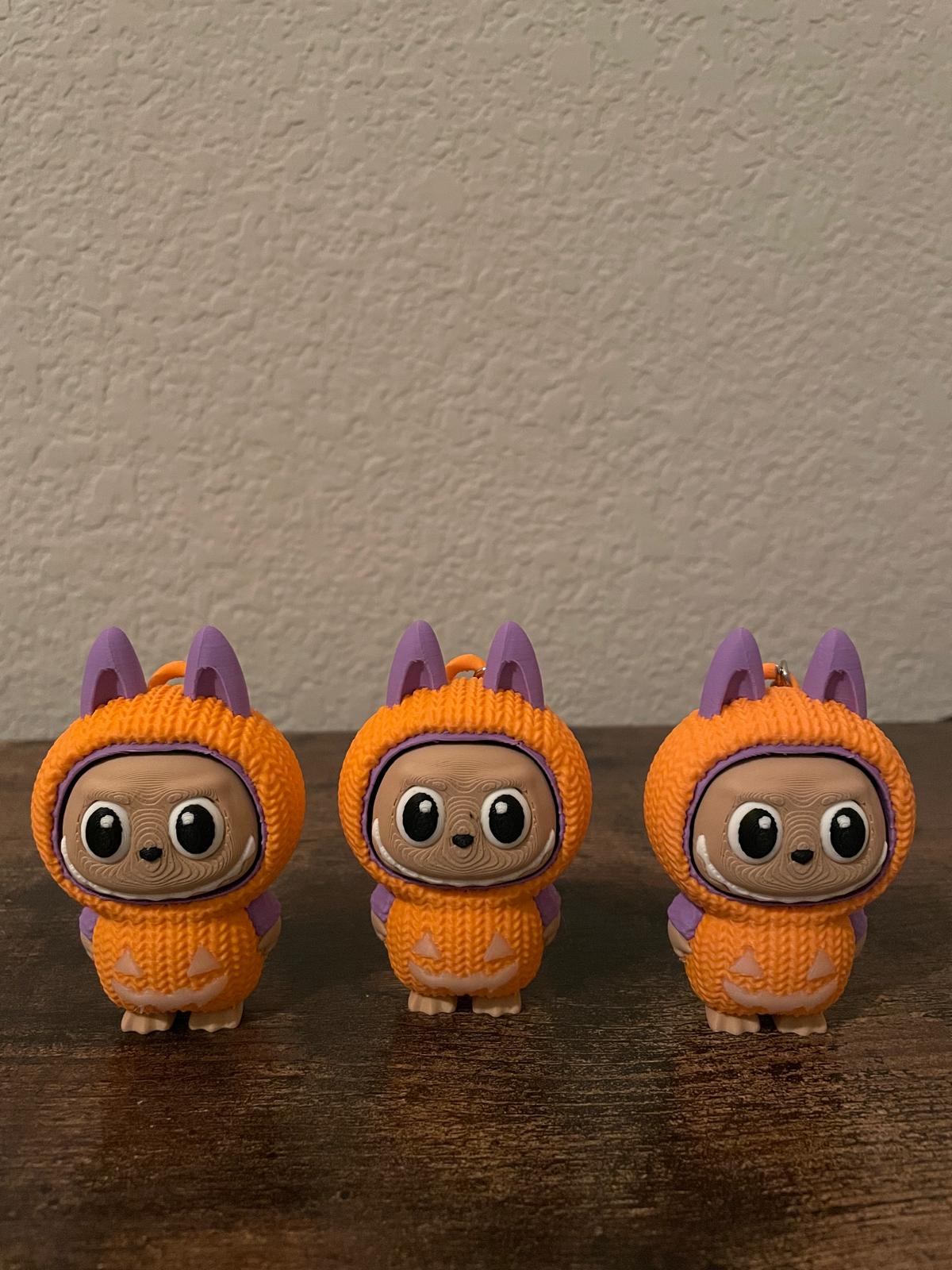 Limited edition Halloween Labubu fidget toy in a pumpkin onesie outfit with jack-o’-lantern details. Cute collectible figure with a clicky face feature, designed for Halloween season décor, stress relief, and toy collectors.