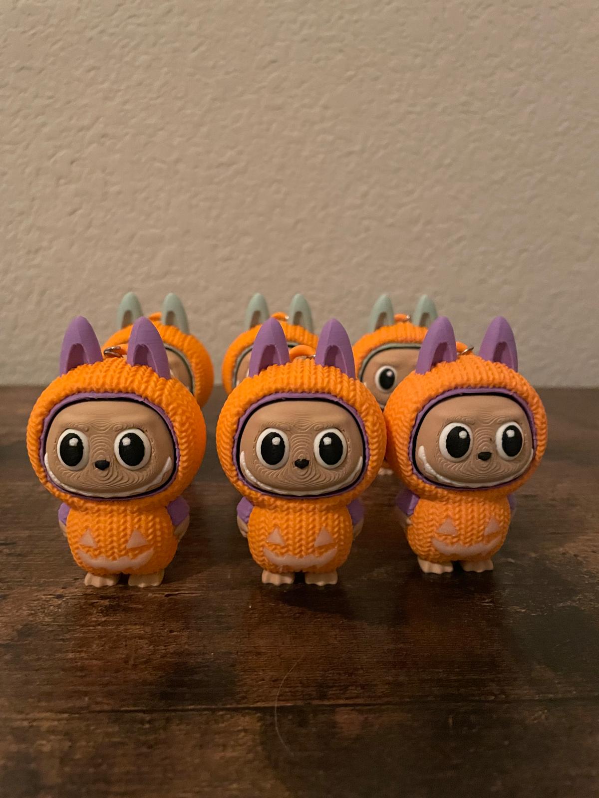 Limited edition Halloween Labubu fidget toy in a pumpkin onesie outfit with jack-o’-lantern details. Cute collectible figure with a clicky face feature, designed for Halloween season décor, stress relief, and toy collectors.