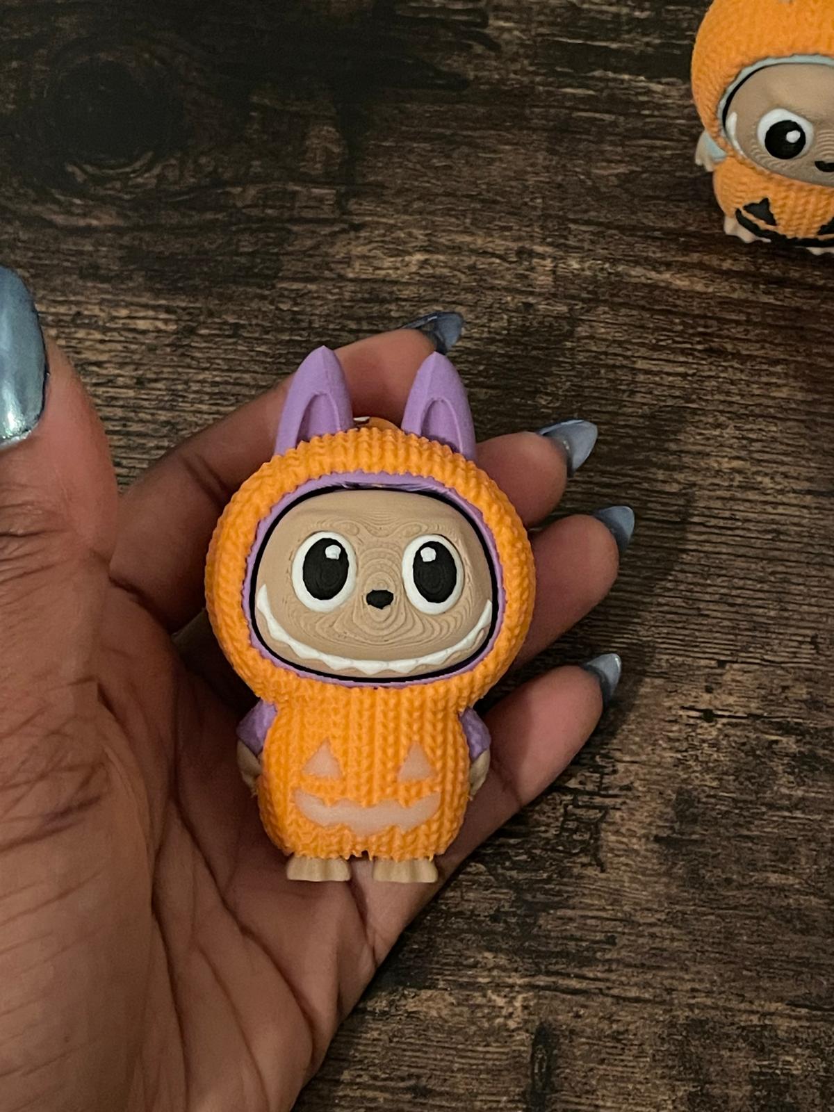 Limited edition Halloween Labubu fidget toy in a pumpkin onesie outfit with jack-o’-lantern details. Cute collectible figure with a clicky face feature, designed for Halloween season décor, stress relief, and toy collectors.