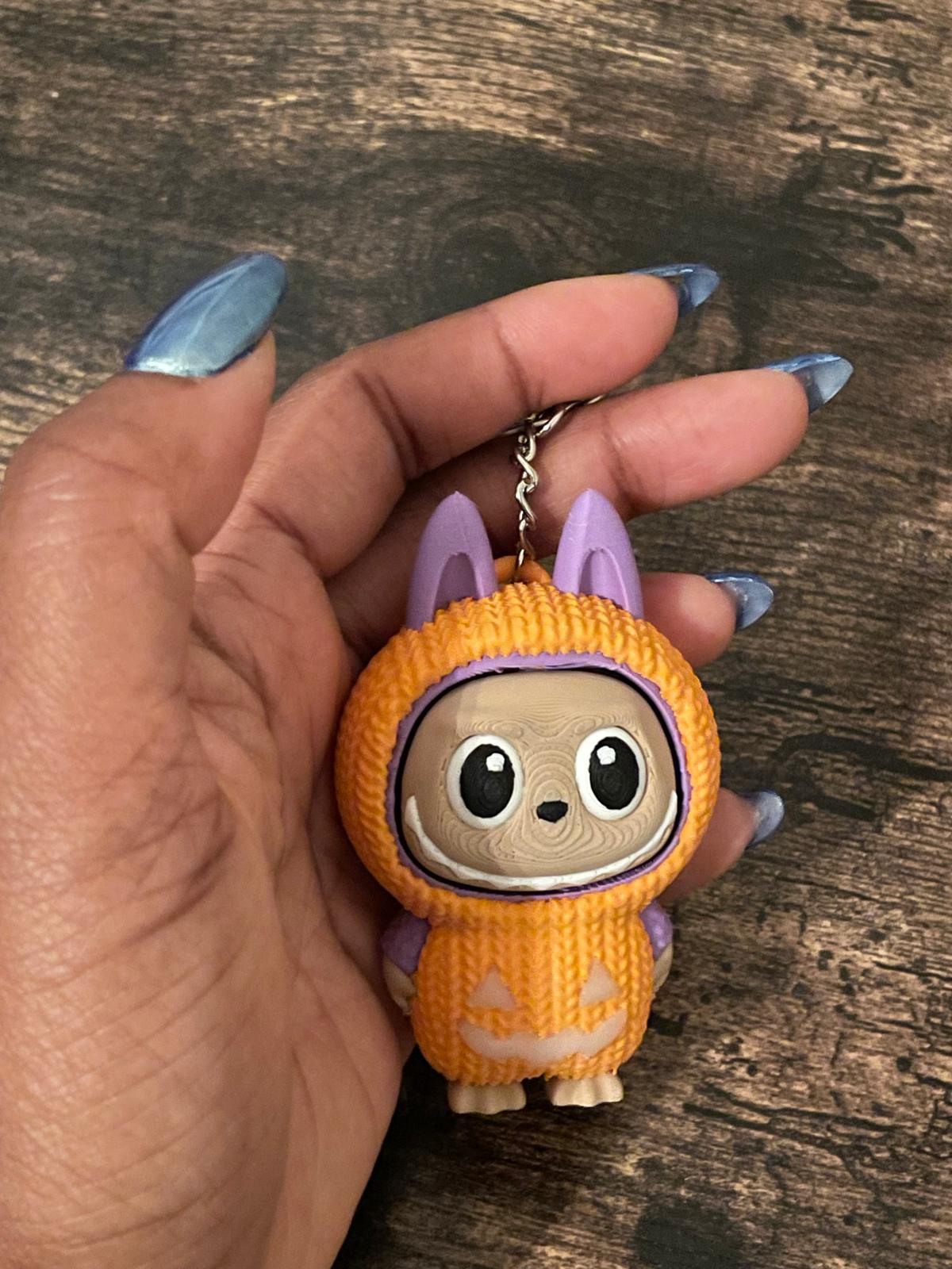 Limited edition Halloween Labubu fidget toy in a pumpkin onesie outfit with jack-o’-lantern details. Cute collectible figure with a clicky face feature, designed for Halloween season décor, stress relief, and toy collectors.